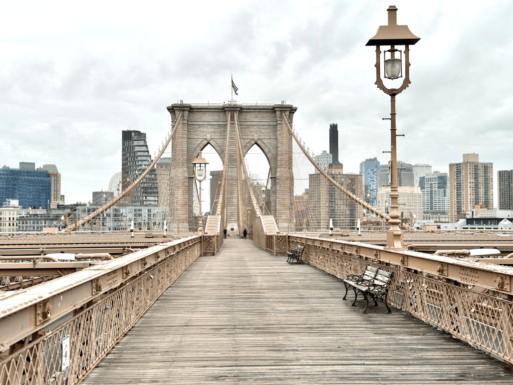 Pedestrian walkway across the Brooklyn Bridge with its stone arches and Manhattan skyline in the distance, perfect for Brooklyn Bridge captions.