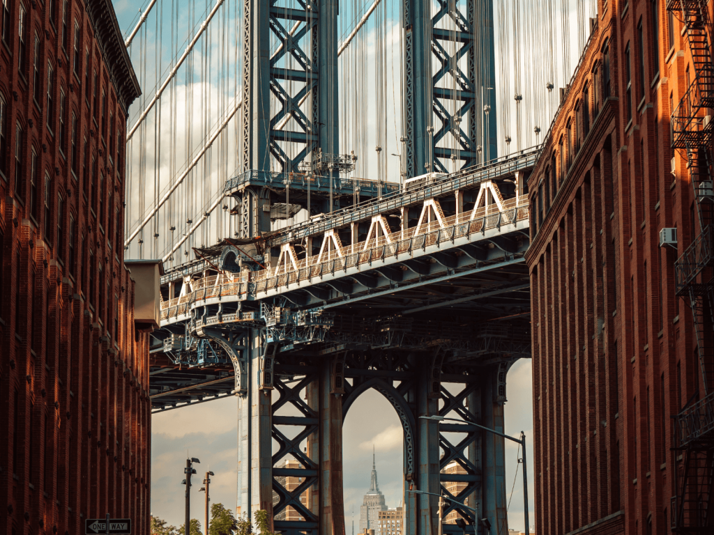 Manhattan Bridge framed by red brick buildings in DUMBO, with the Empire State Building visible in the distance.