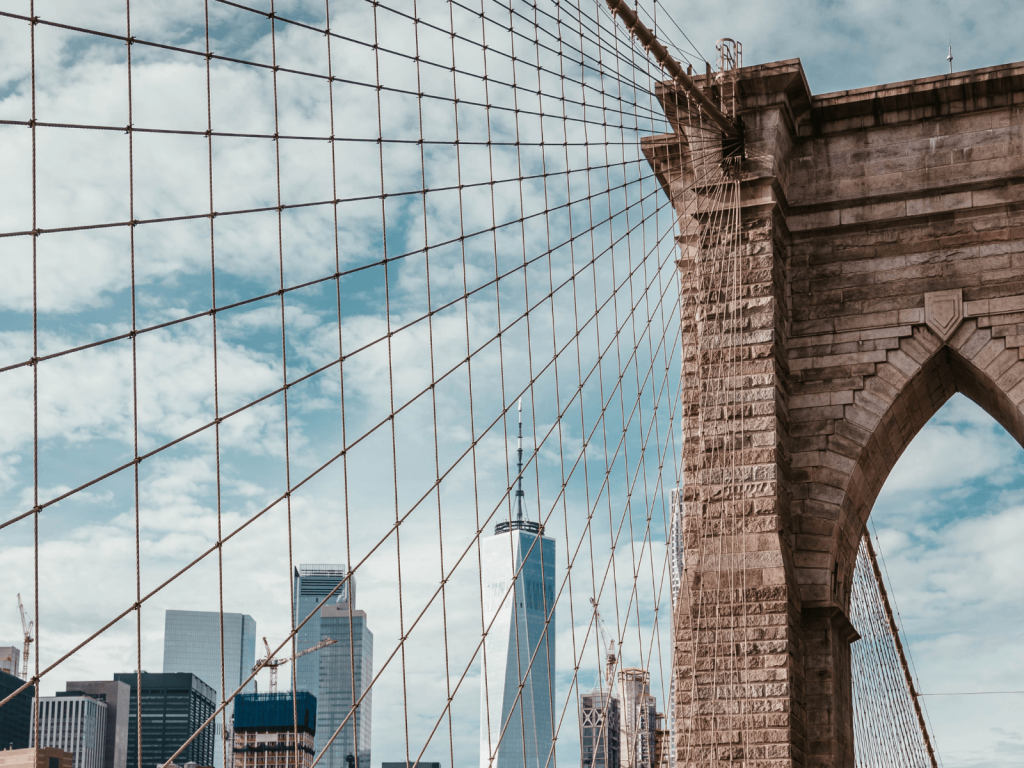 Close up view of the Brooklyn Bridge cables and stone tower with One World Trade Center visible in the background.