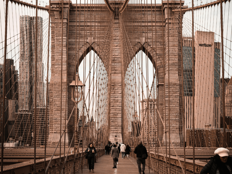 Pedestrians walking across the Brooklyn Bridge beneath its stone arches and suspension cables, perfect for Brooklyn Bridge captions.