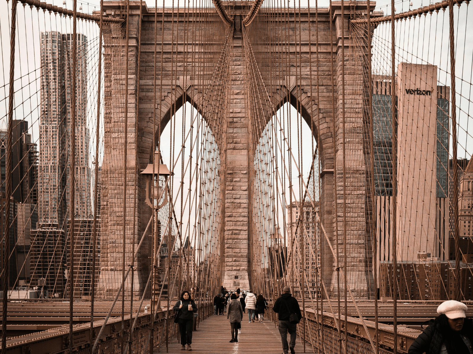 Pedestrians walking across the Brooklyn Bridge beneath its stone arches and suspension cables, perfect for Brooklyn Bridge captions.