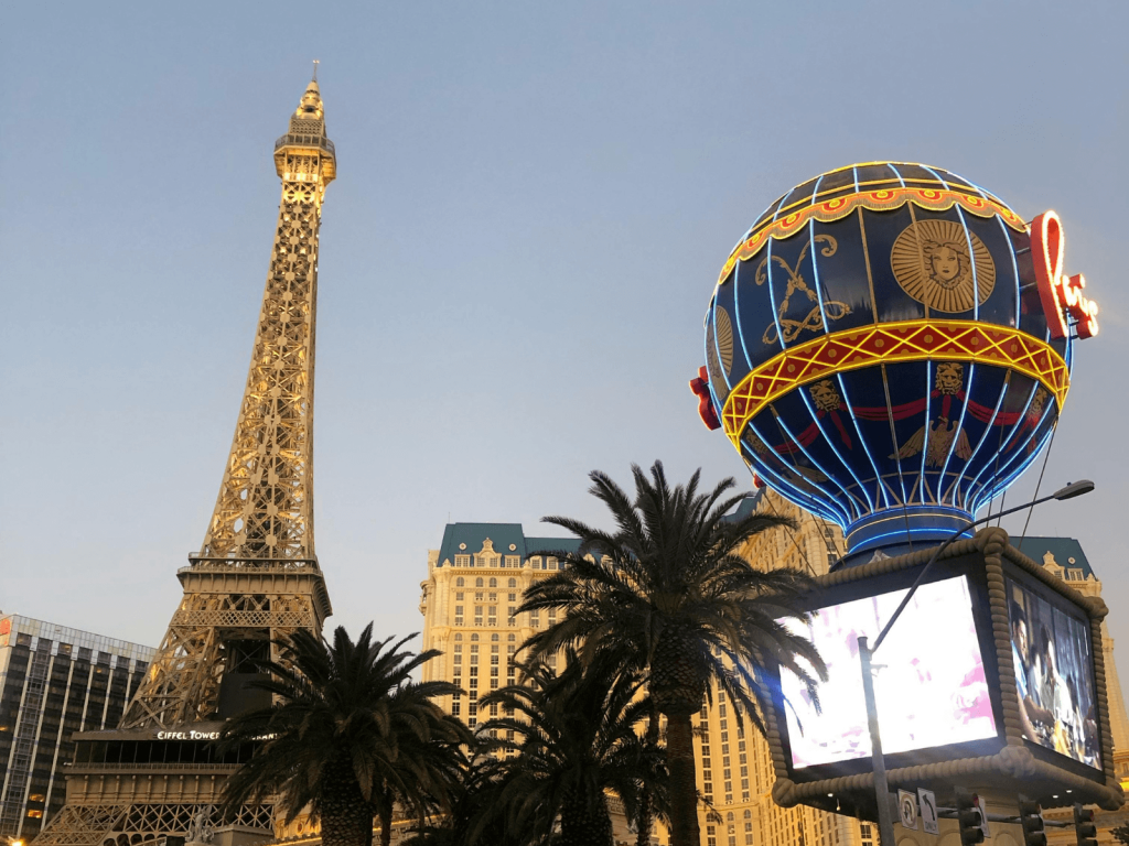 Eiffel Tower replica and illuminated Paris Las Vegas balloon rising above palm trees along the Las Vegas Strip.