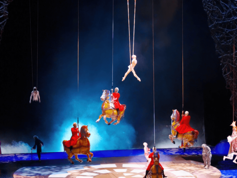 Aerial performers and riders on suspended carousel horses during a colorful Las Vegas stage show, perfect for Las Vegas captions.