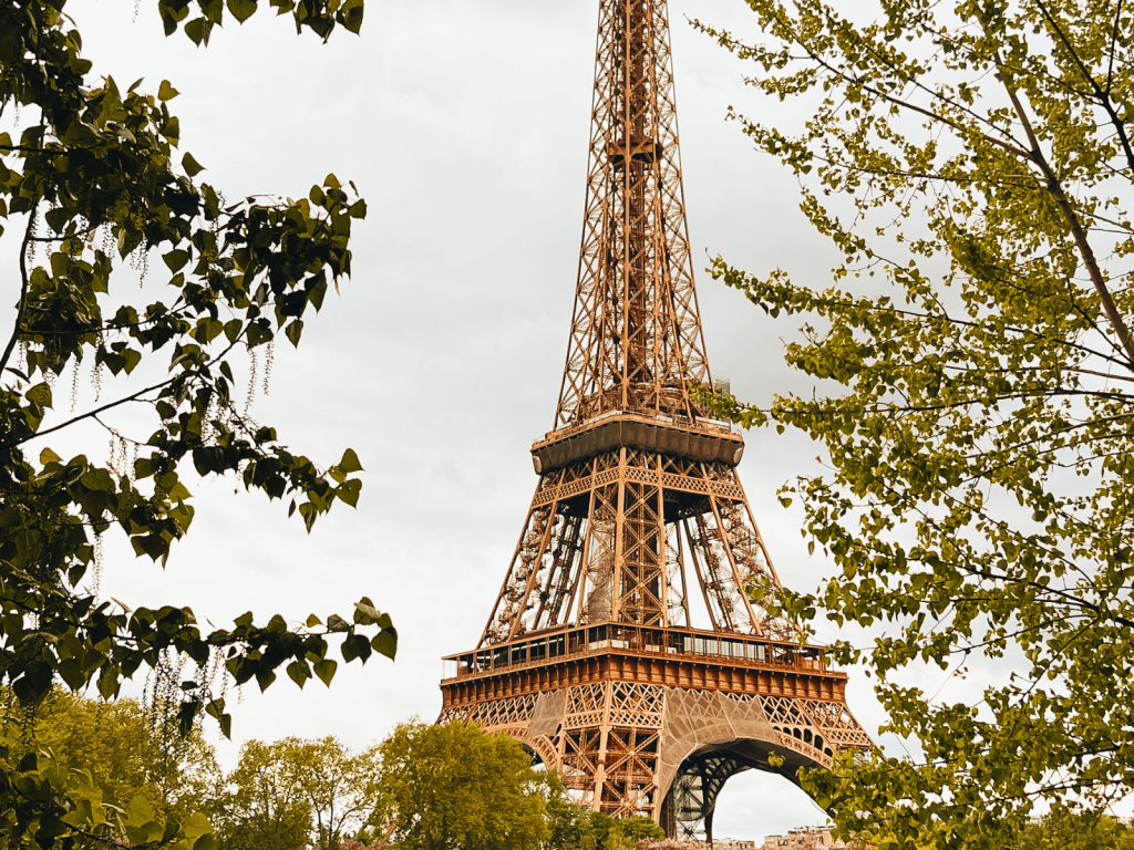 The Eiffel Tower framed by leafy green trees against an overcast Paris sky, perfect for Paris Instagram captions.