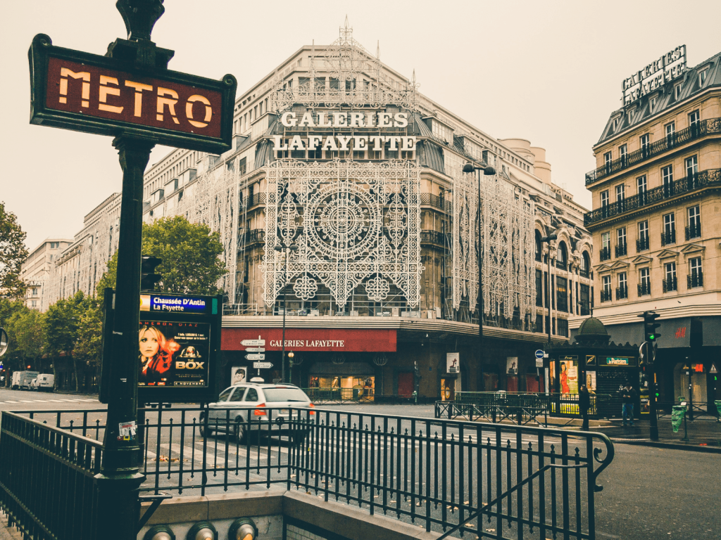 Paris Métro entrance sign in front of Galeries Lafayette and classic Haussmann style buildings in central Paris.