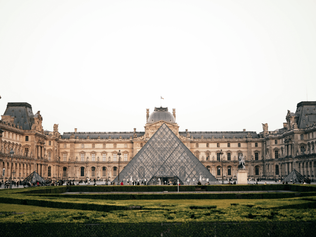 The glass Louvre Pyramid surrounded by the historic Louvre Palace and manicured gardens in Paris, perfect for Paris Instagram captions.