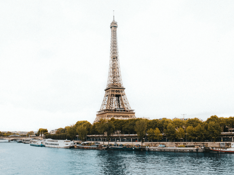 Eiffel Tower viewed across the Seine River with boats along the waterfront and autumn trees, a classic Paris scene for Paris Instagram captions.