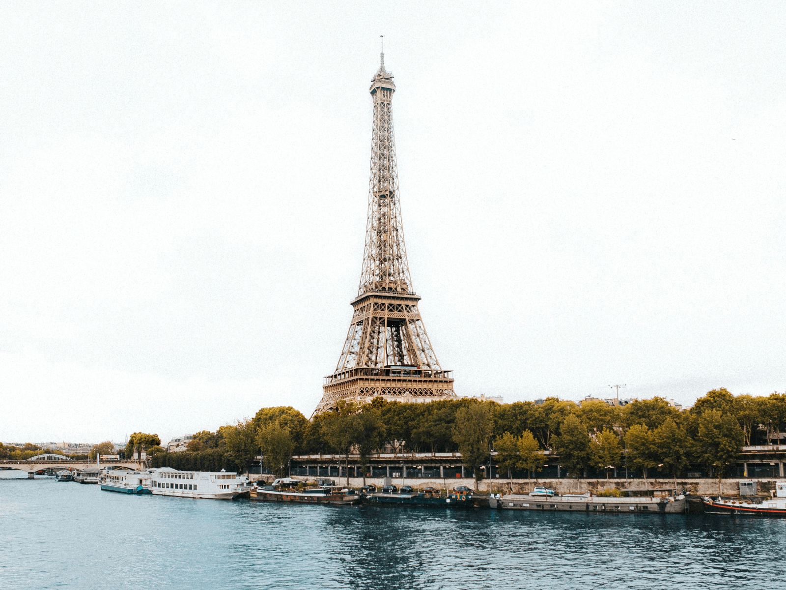 Eiffel Tower viewed across the Seine River with boats along the waterfront and autumn trees, a classic Paris scene for Paris Instagram captions.