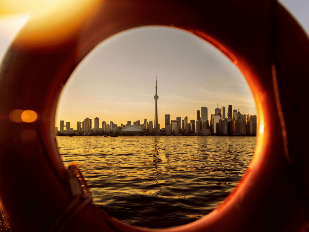 Toronto skyline and CN Tower glowing at sunset across Lake Ontario, framed through a circular opening, perfect for Toronto captions.