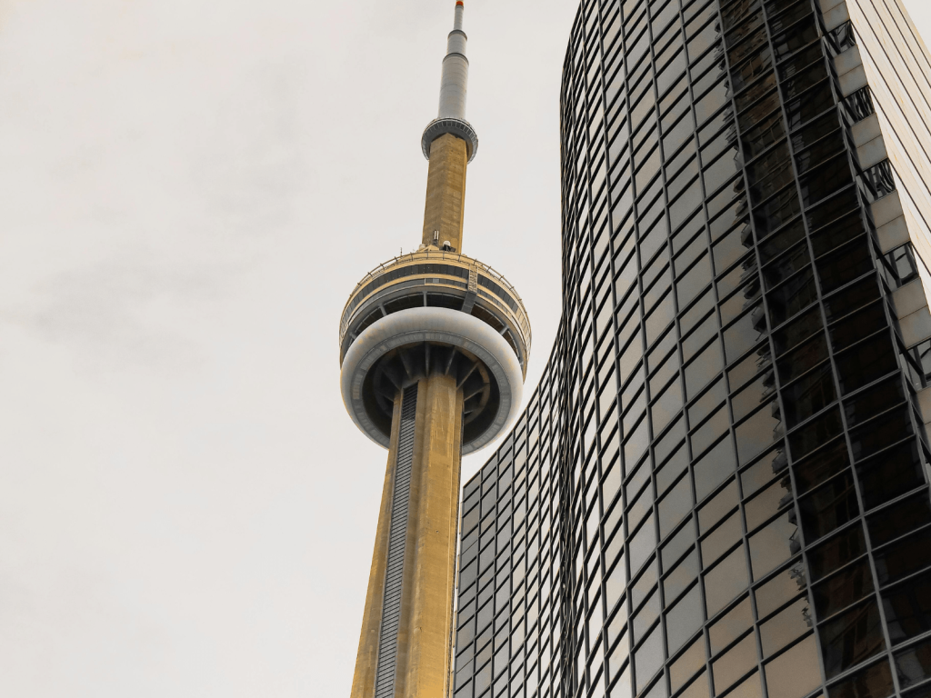 Low angle view of the CN Tower rising beside a modern glass building in downtown Toronto, perfect for Toronto captions.