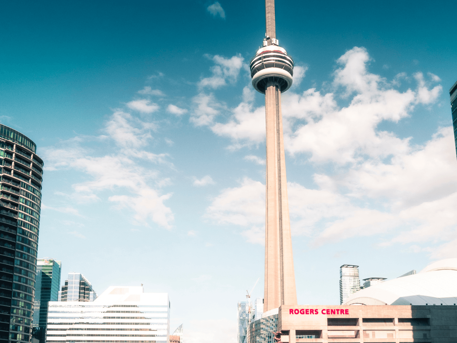 CN Tower rising above the Rogers Centre and downtown Toronto buildings under a bright blue sky, perfect for Toronto captions.