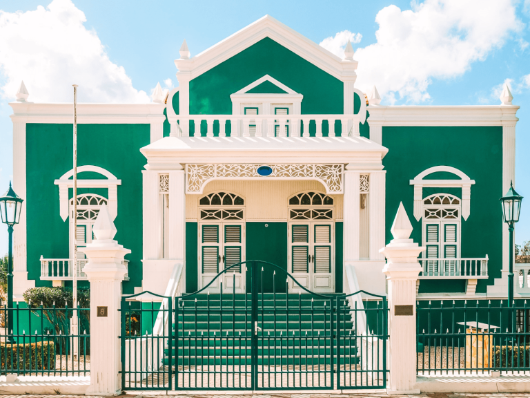 Bright green and white Dutch colonial building beneath a blue sky on one of the ABC Islands in the Caribbean.