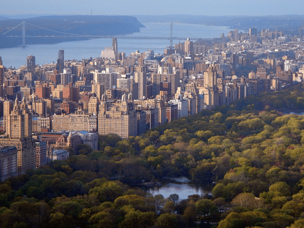 Aerial view over Central Park with the Manhattan skyline, Hudson River, and George Washington Bridge in the distance, perfect for Central Park captions.