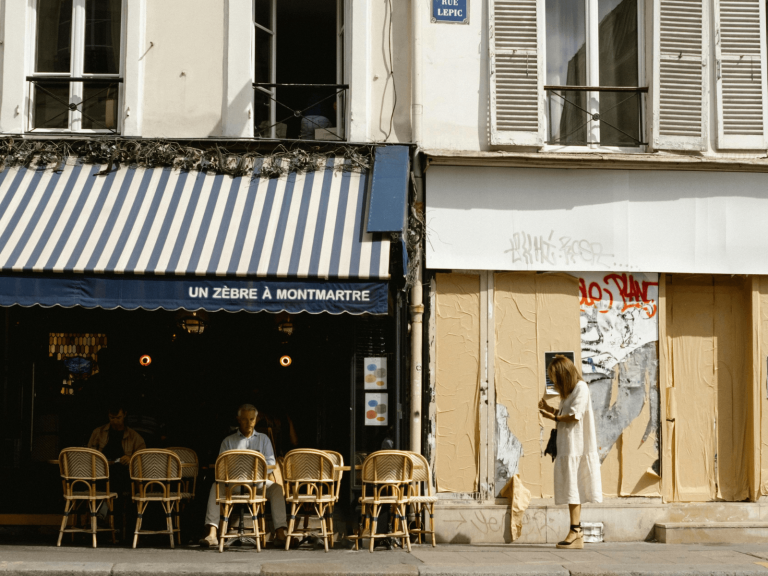 Sidewalk seating outside a charming Paris cafe with striped awnings and classic woven bistro chairs in Montmartre, perfect for discovering cute cafes in Paris.