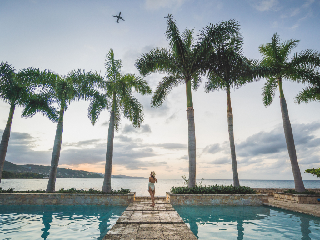 Woman standing between palm trees and resort pools overlooking the ocean in Jamaica.