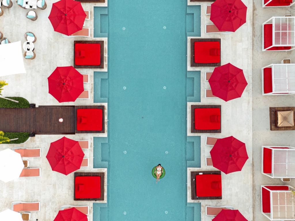 Overhead view of a resort swimming pool surrounded by bright red umbrellas and lounge beds.