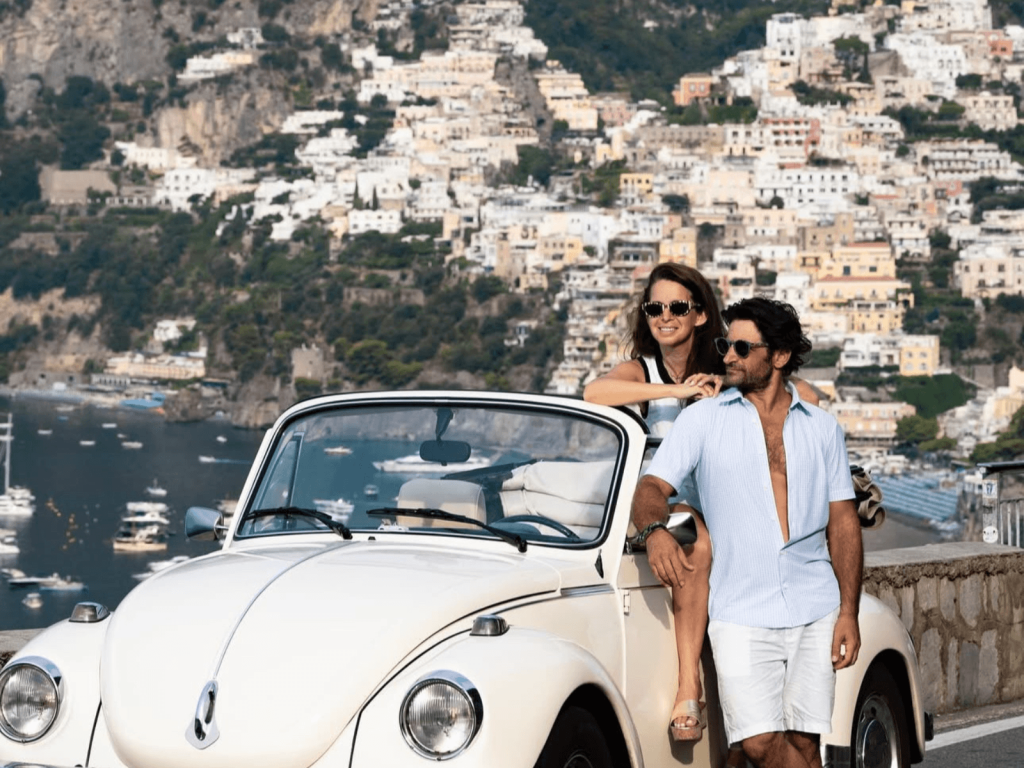 Couple posing beside a white vintage convertible overlooking Positano and the Amalfi Coast, perfect for Italy Instagram captions.