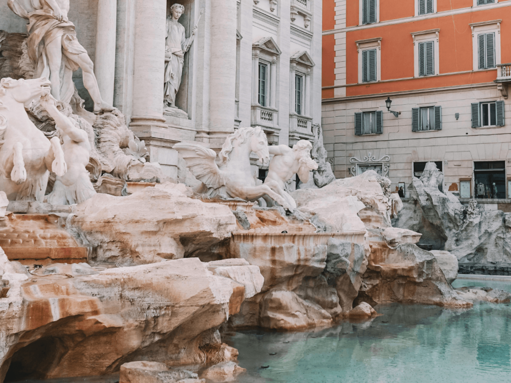 Detailed view of the Trevi Fountain in Rome with white marble sculptures, turquoise water, and historic buildings.
