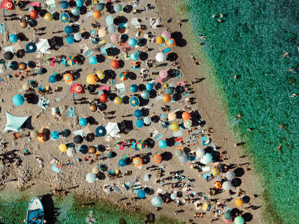 Aerial view of a busy Italian beach filled with colorful umbrellas beside clear turquoise water.
