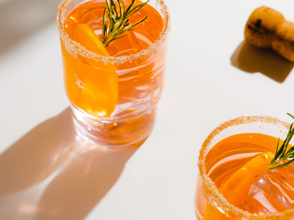 Two orange cocktails with sugared rims, citrus slices, and rosemary garnishes, ideal for cocktail captions for Instagram.