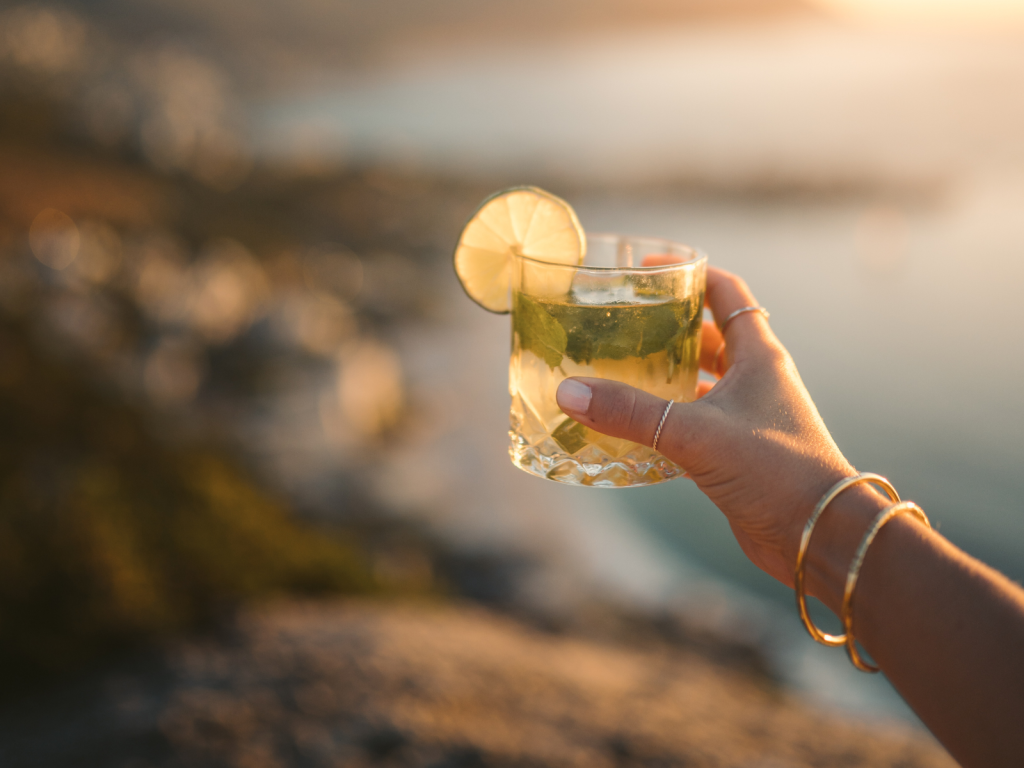Woman holding a refreshing cocktail with lime and mint outdoors during golden hour, perfect for cocktail captions for Instagram.