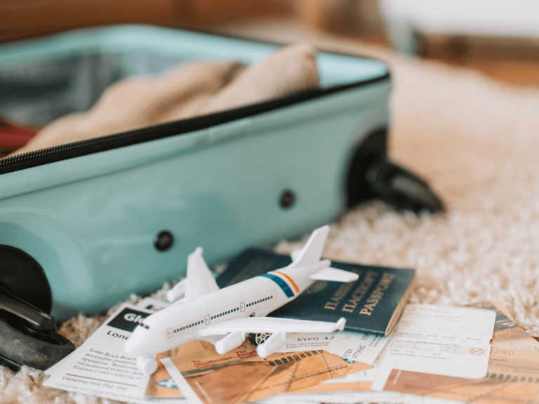 Open turquoise suitcase with a toy airplane, passport, boarding pass, and travel documents showing what to pack for a long flight.