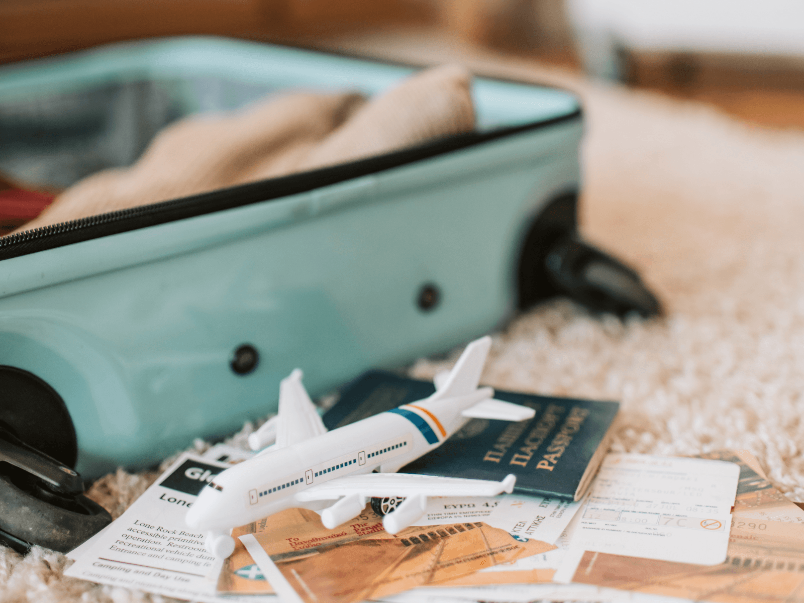 Open turquoise suitcase with a toy airplane, passport, boarding pass, and travel documents showing what to pack for a long flight.