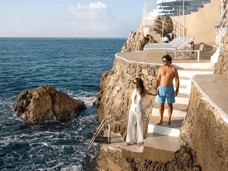 Couple holding hands on stone steps beside the ocean for two word captions for couples.