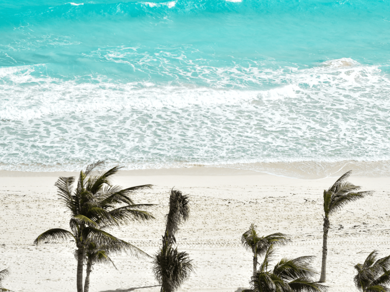 Aerial view of a white sand beach lined with palm trees and bright turquoise waves in Cancun, Mexico, for a post about Cancun Instagram captions.