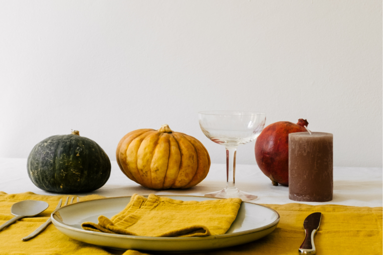 Autumn table setting with pumpkins, pomegranate, candle, and cocktail glass, perfect inspiration for fall cocktail recipes.