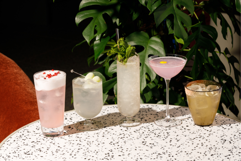 Colorful cocktails in different glasses on a table with tropical greenery, perfect inspiration for drinking captions.