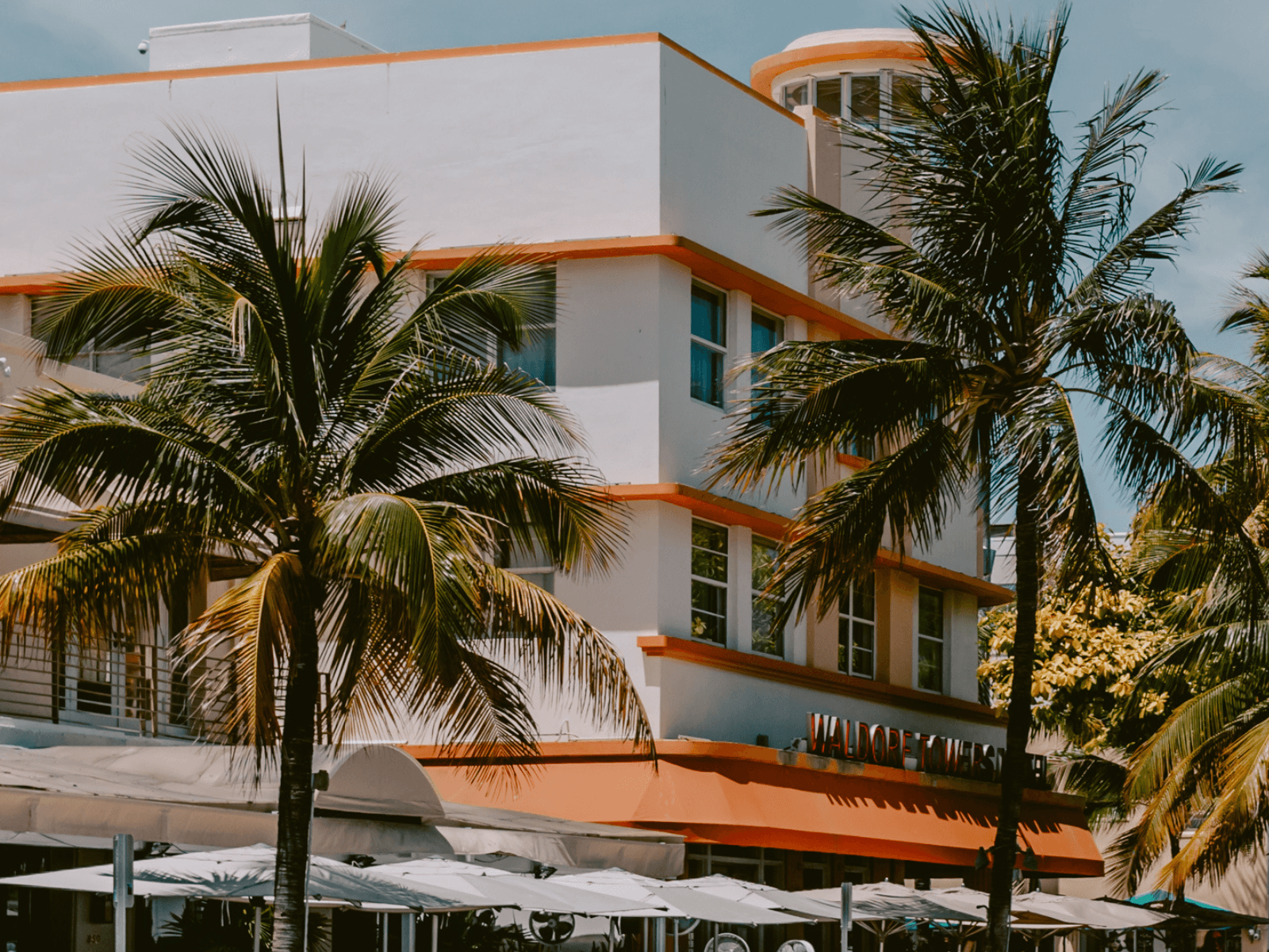 Palm trees frame a white Art Deco building with orange trim on a sunny day in Miami.