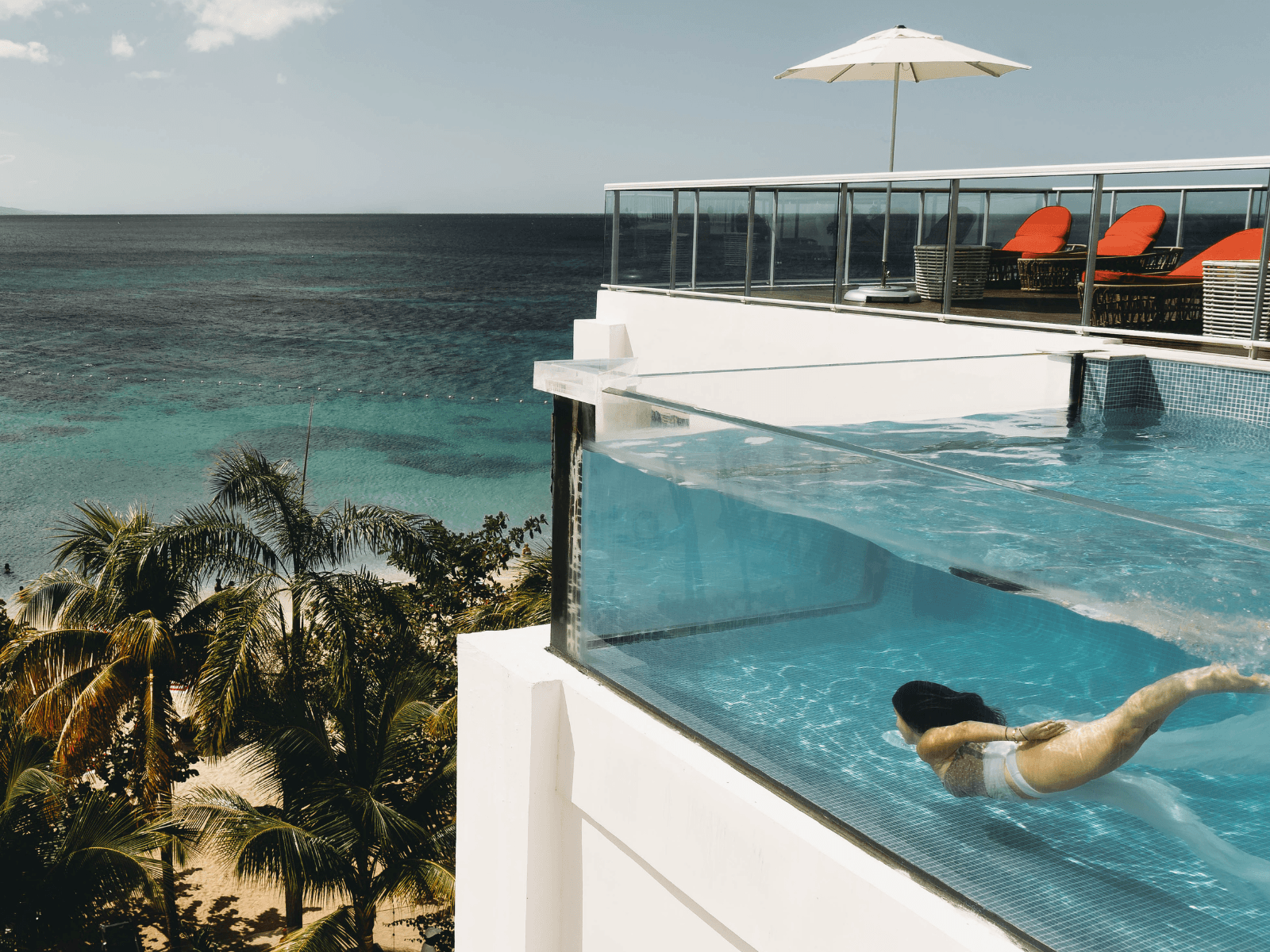 Woman swimming underwater in a rooftop infinity pool overlooking palm trees and the turquoise Caribbean Sea for a post about tropical captions.