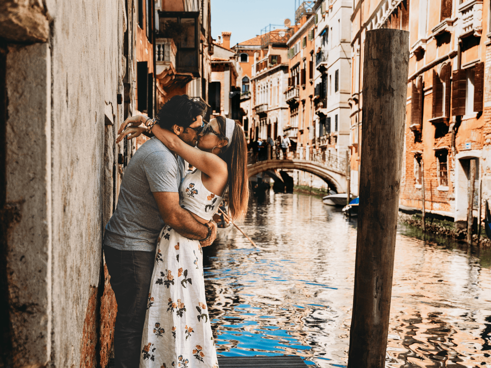 Couple kissing beside a picturesque canal lined with historic buildings and a small bridge in Venice, Italy, for a post about Venice Instagram captions.