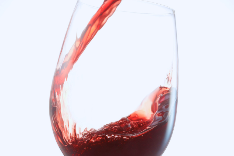 Red wine being poured into a wine glass against a bright white background for a collection of wine captions.