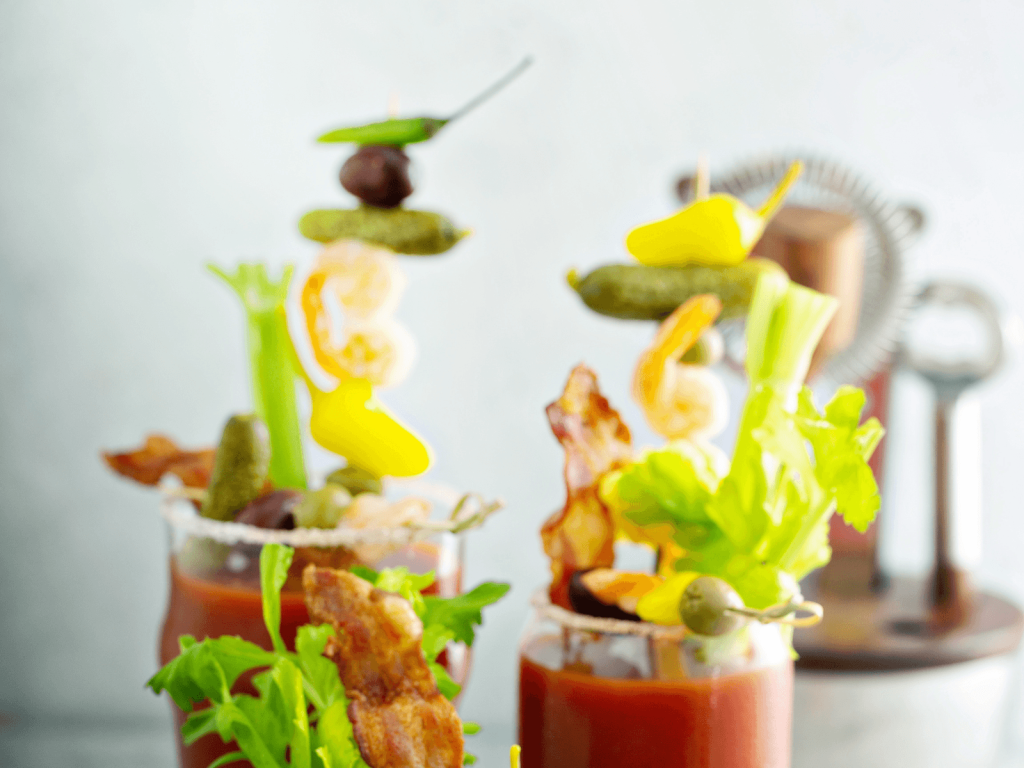 Bloody Mary cocktails topped with celery, pickles, olives, shrimp, bacon, and other savory garnishes.