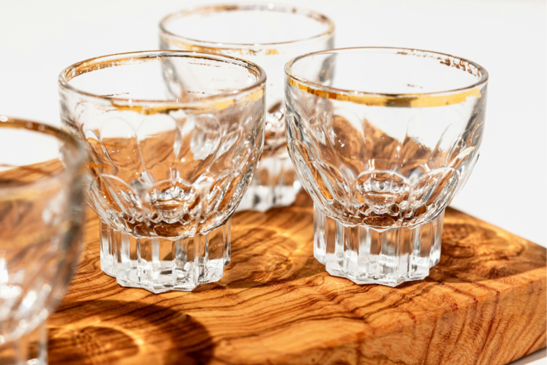 Crystal shot glasses with gold rims displayed on a wooden board for a collection of tequila captions.