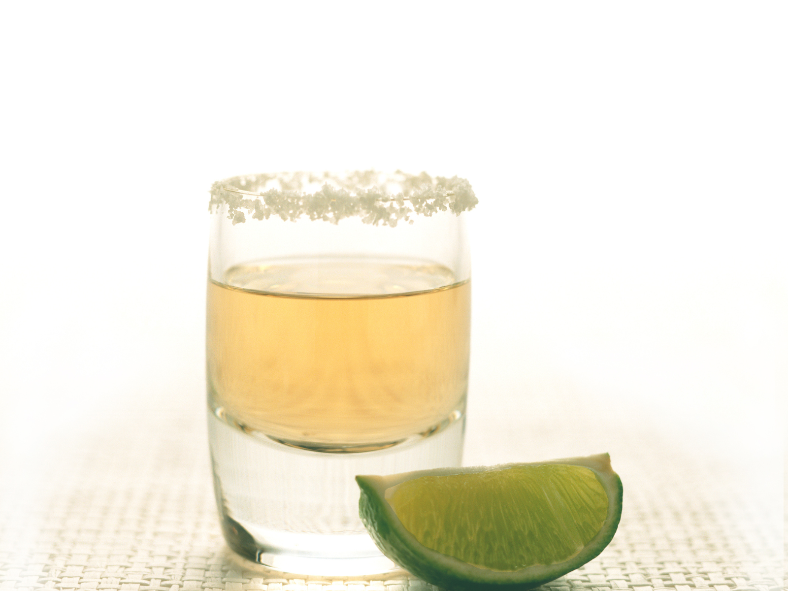 Tequila captions photo of a salt rimmed shot of tequila with a lime.