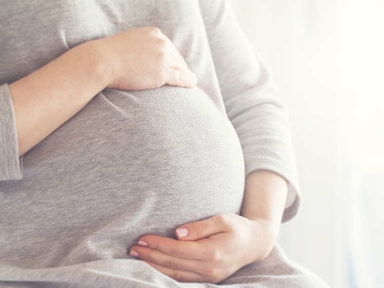 Pregnant woman gently holding her baby bump for a maternity bag checklist.