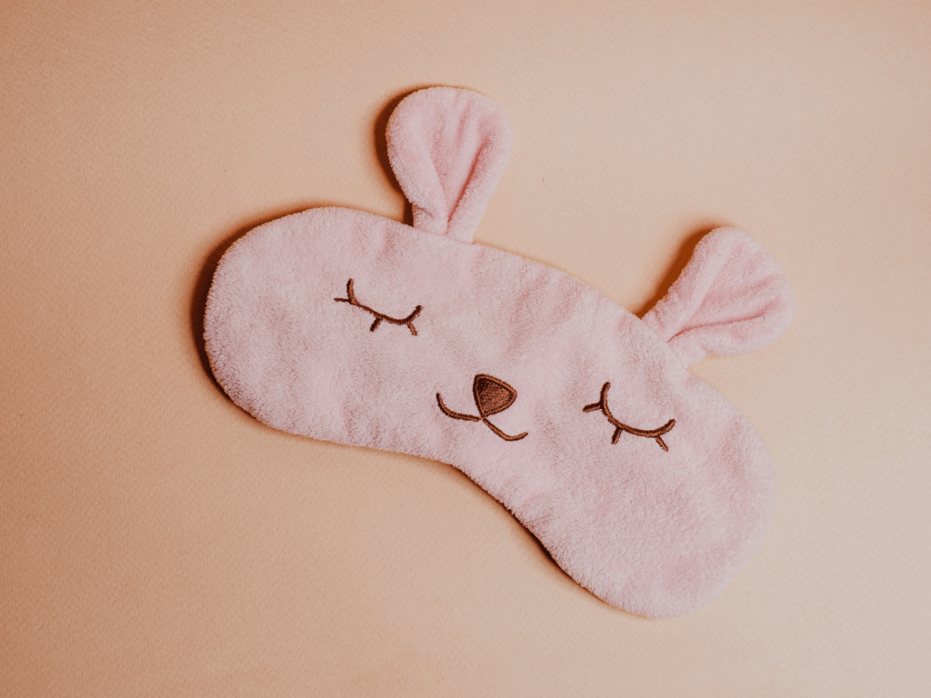 Soft pink animal shaped sleep mask with embroidered closed eyes and ears, a cozy item to include on a maternity bag checklist
