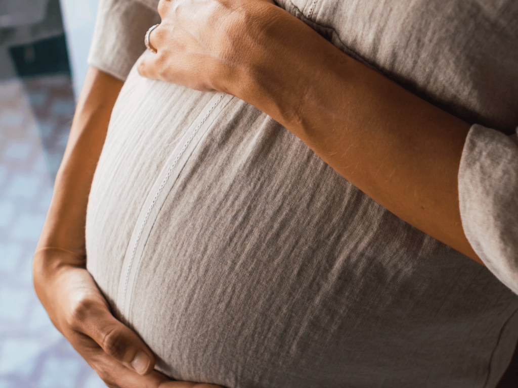 Close up of a pregnant woman cradling her belly with both hands, preparing for birth with a maternity bag checklist.