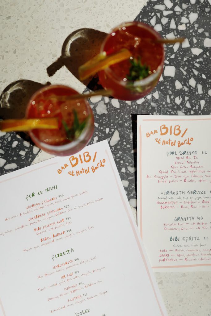 Overhead photo of stylish cocktails and a handwritten bar menu from Hotel Bardo, showcasing local flair and design-forward details.