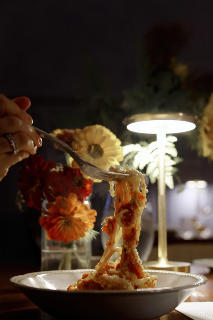 A close-up of someone twirling pasta under soft lamplight with flowers in the background — a romantic dinner scene that defines the charm of 2 days in Savannah, Georgia.