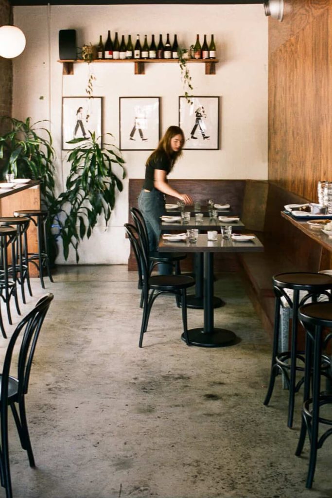 A cozy restaurant interior with modern artwork, plants, and a server setting tables — warm and inviting Savannah dining vibes.