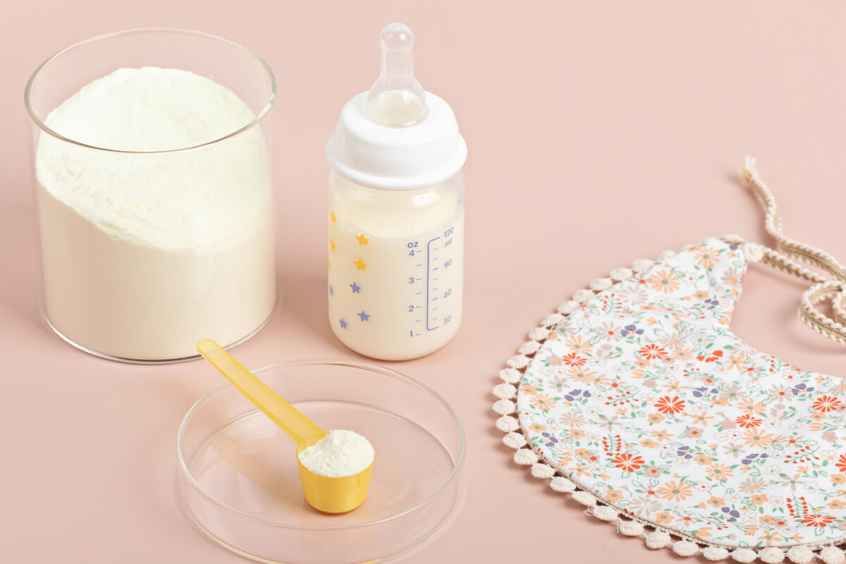 A baby bottle filled with milk, a scoop of powder, and a floral bib arranged neatly on a pastel background, featuring the Best Organic Baby Formula for infants.
