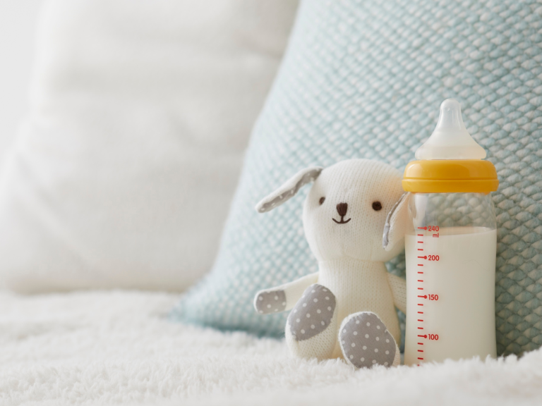 Baby bottle filled with formula beside a soft stuffed toy on a blanket for a guide to the best organic baby formula.