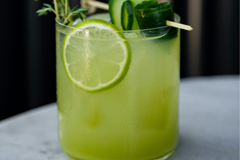 Cucumber basil gimlet cocktail garnished with fresh cucumber, lime, and herbs in a glass.