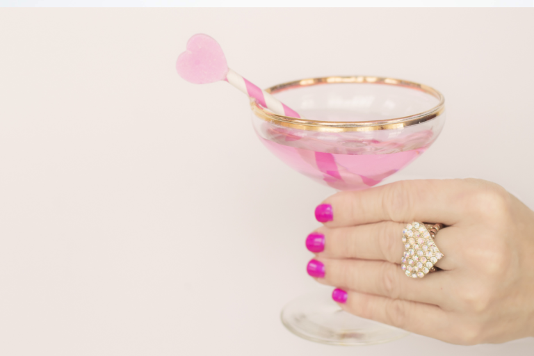 Pink Valentine cocktail in a gold rimmed coupe glass with a heart shaped stirrer to showcase Valentine cocktails.