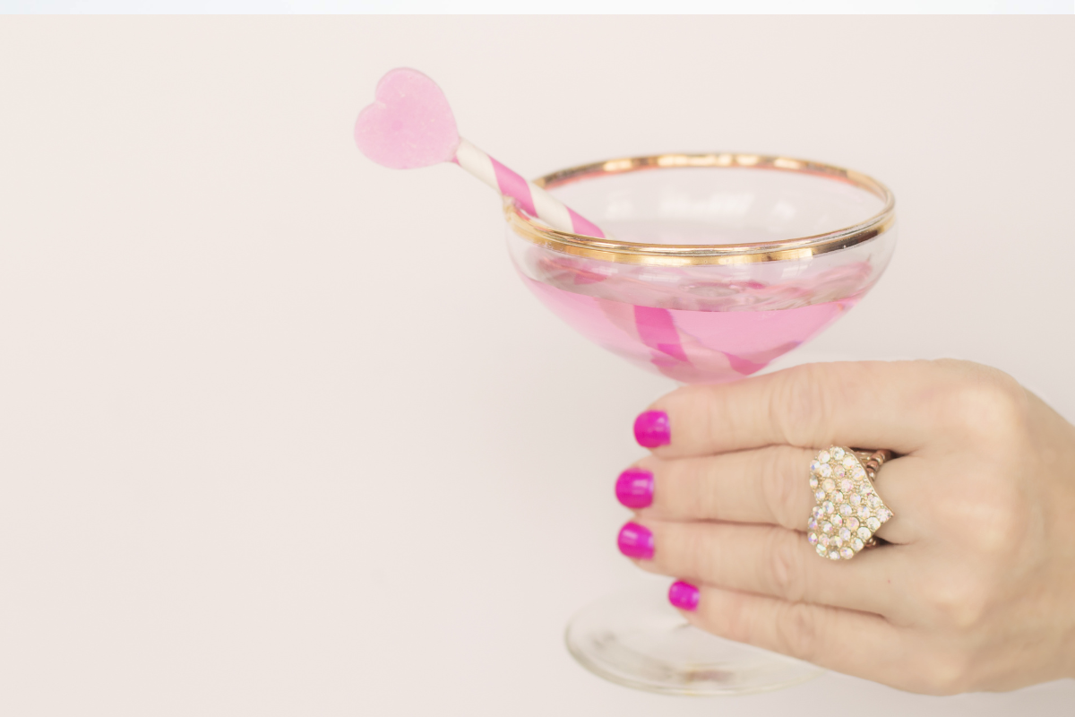 Pink Valentine cocktail in a gold rimmed coupe glass with a heart shaped stirrer to showcase Valentine cocktails.
