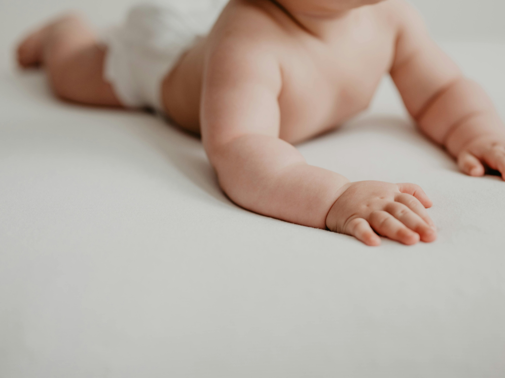 Close up of a baby lying on a white changing surface wearing a diaper, representing everyday newborn diaper bag essentials for changing a baby while away from home.